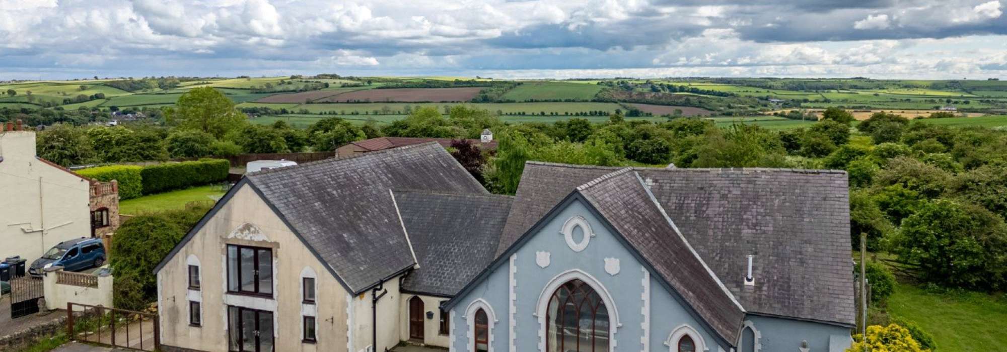 An aerial image of a blue house and white house with a green landscape in the background.