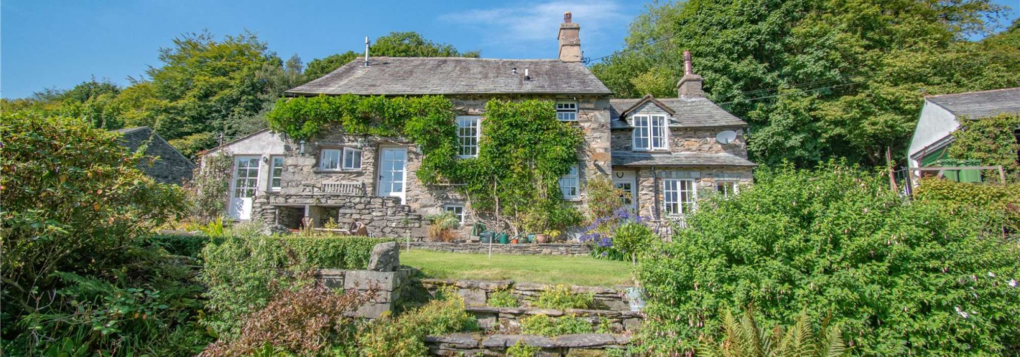 Big brown house surrounded by greenery and a bright blue sky.