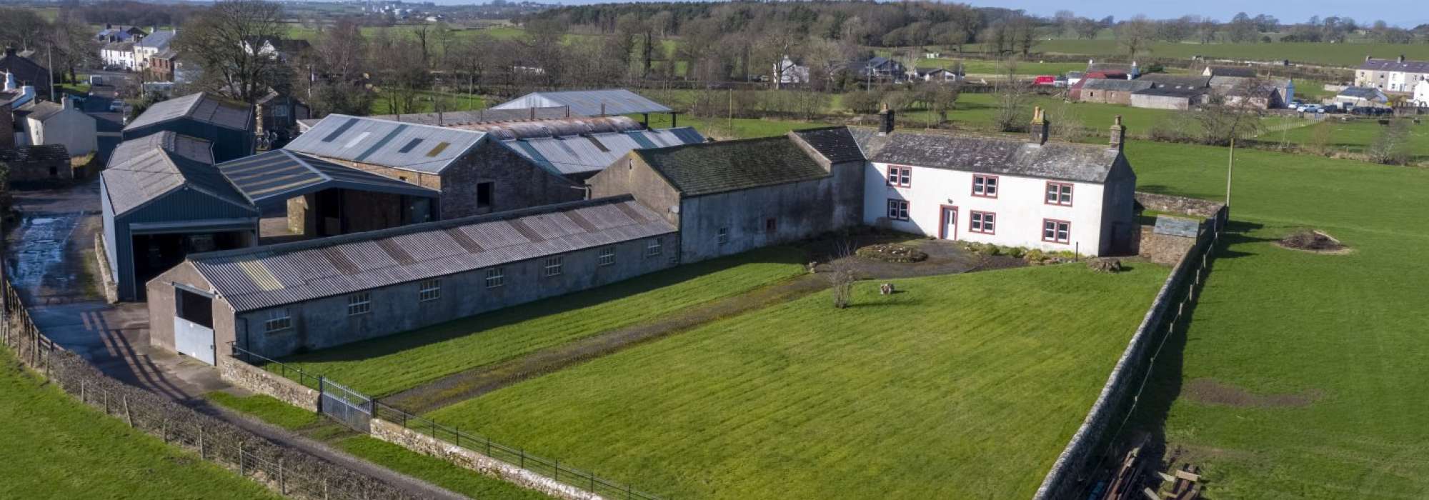 White farmhouse beside sheds surrounded by land. 