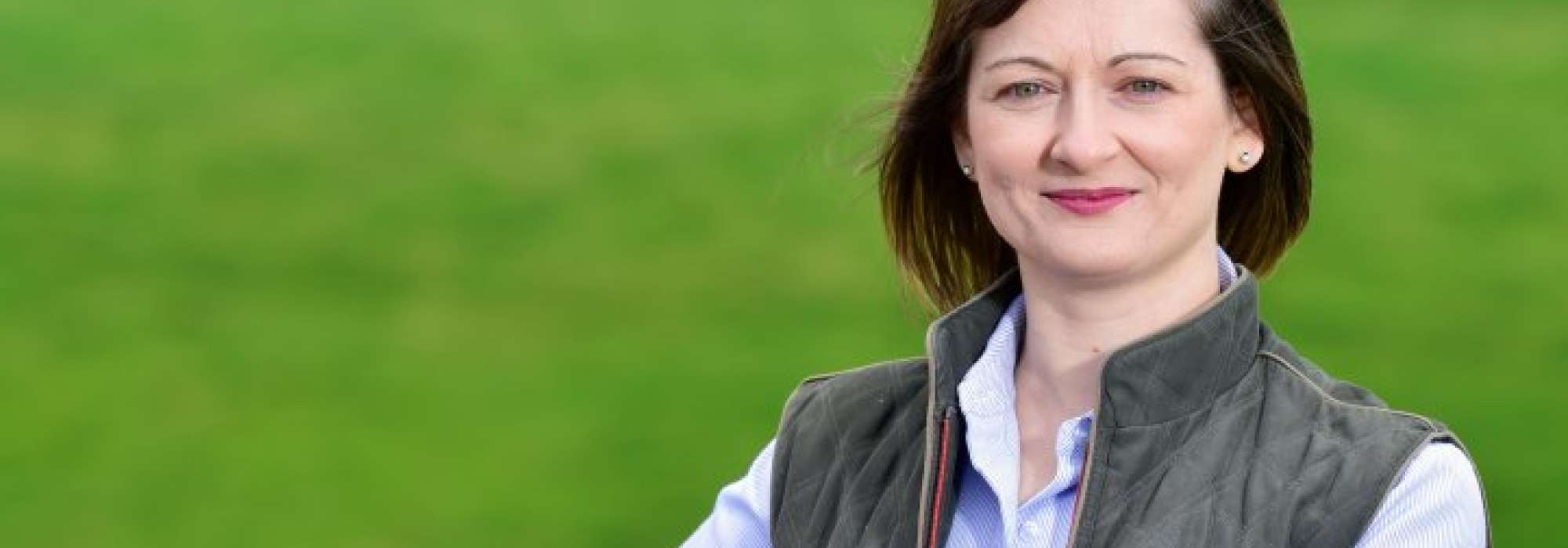 Tracey Jackson,  Head of Environment & Forestry, pictured in a field holding onto a wall.