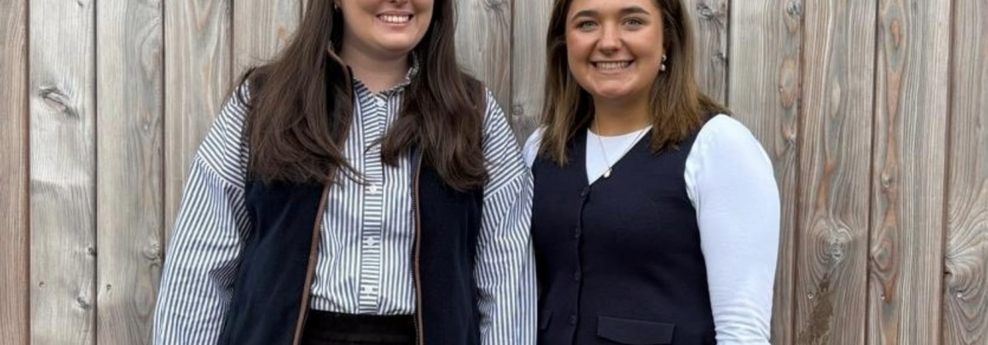 Two women standing in front of a wooden fence